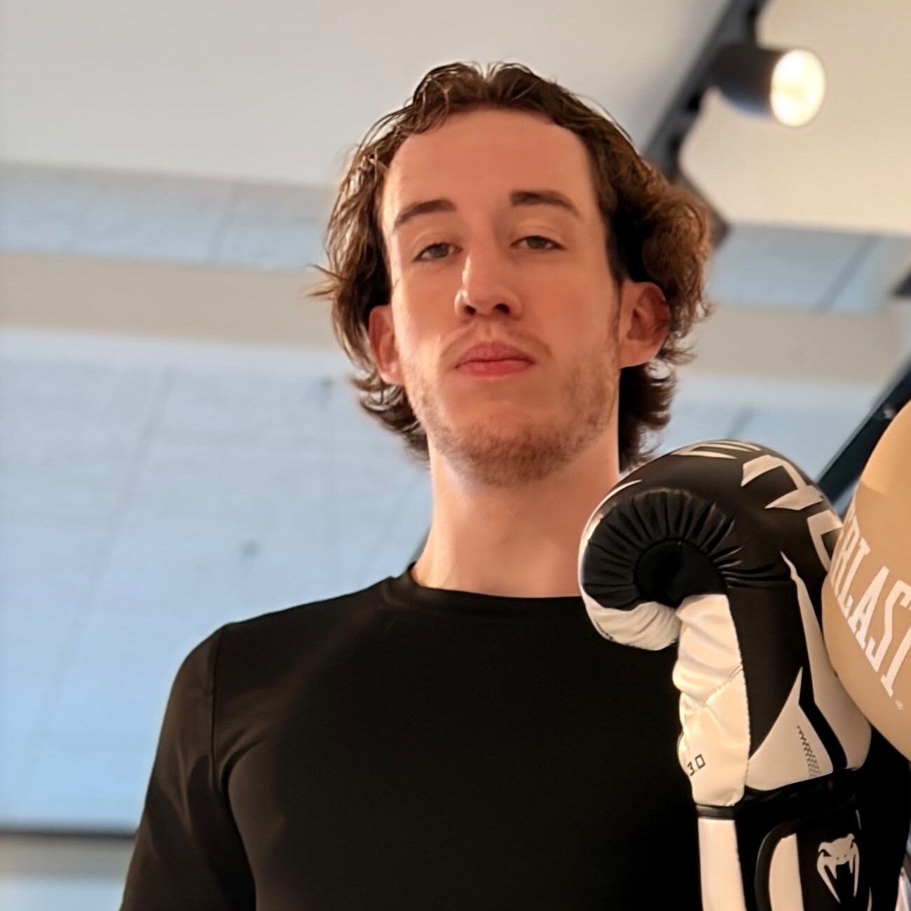 Sven in zwart shirt met een bokshandschoen omhoog in de boksschool