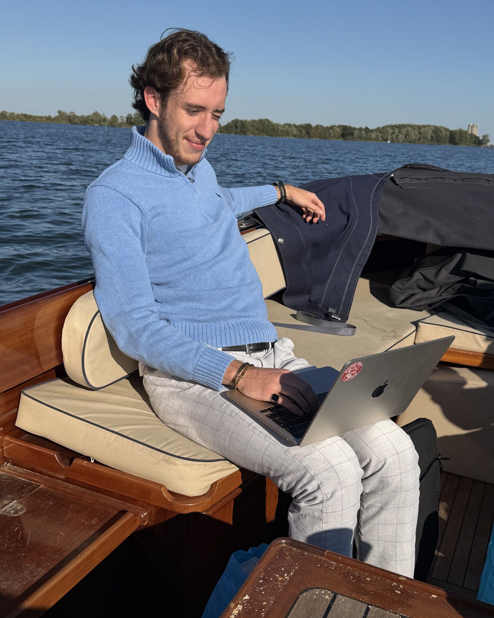 Sven met een laptop op schoot achter in een houten sloep op het water