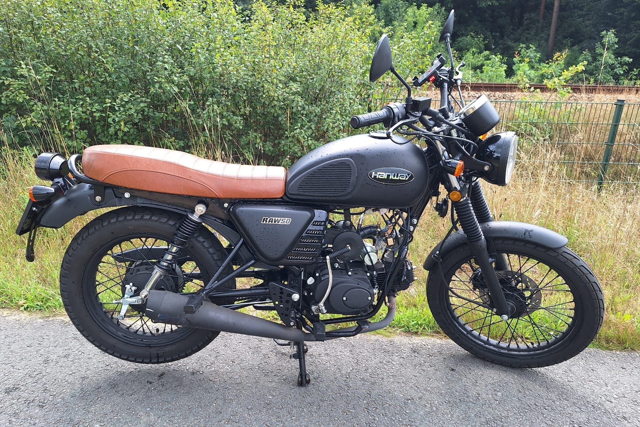 Zijaanzicht van een matzwarte retrobrommer met bruin zadel op een fietspad