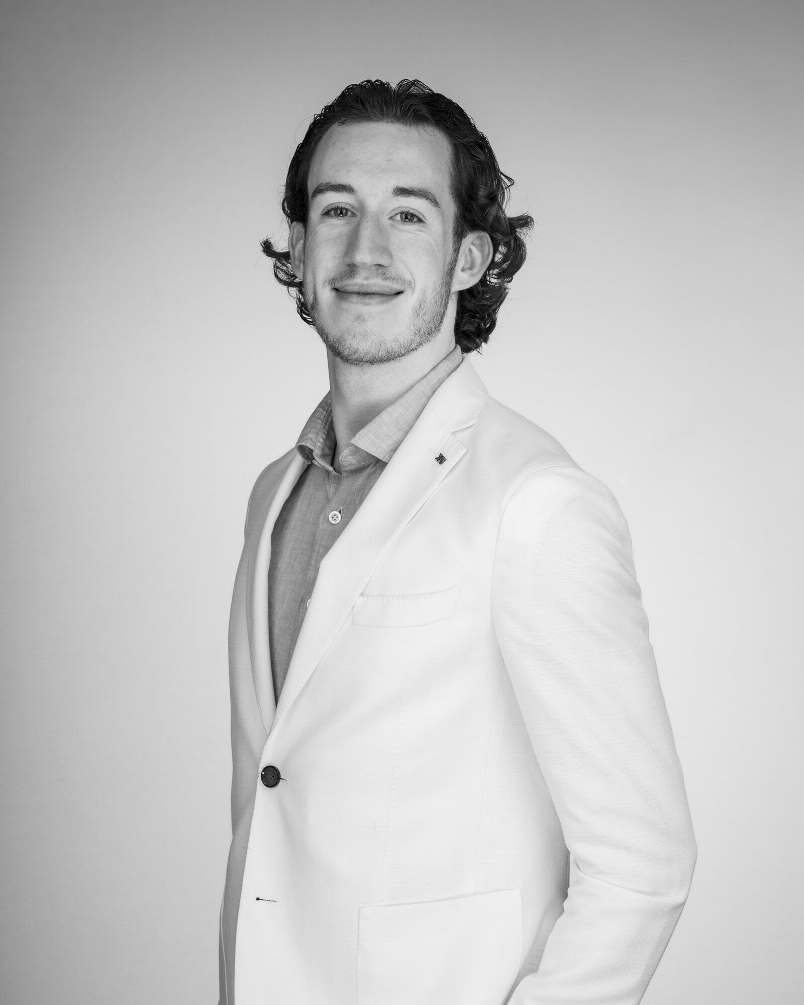 Zwart-witportret van Sven Bakkenes in een wit colbert, glimlachend, met een hand in zijn broekzak